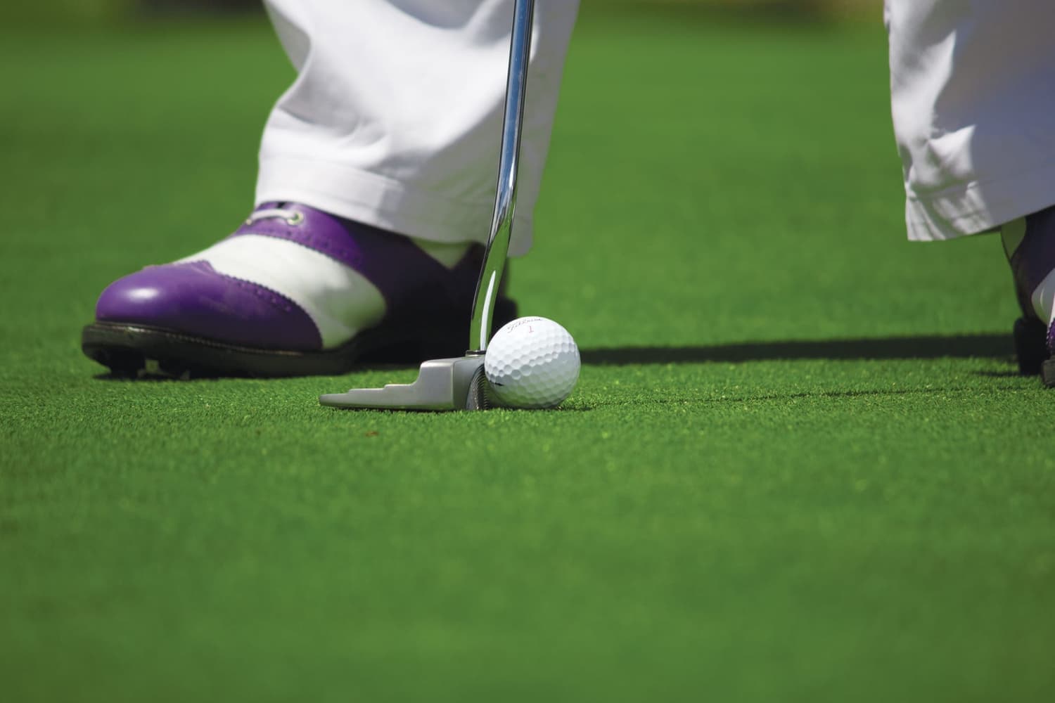 A golfer walking the fairway in golf shoes on green grass