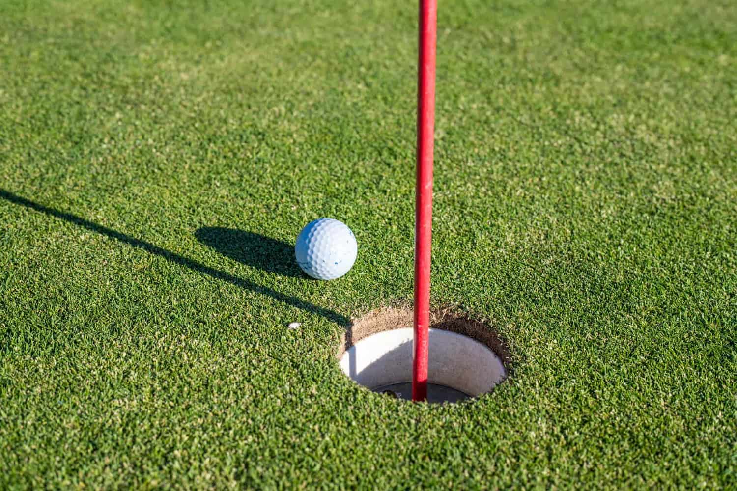 A golf ball beside the hole on a smooth putting green